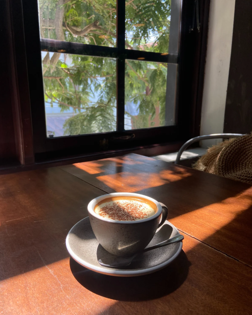 Mujer sentada por la mañana en la mesa de la cocina con una taza de café a la luz del sol frente a una ventana